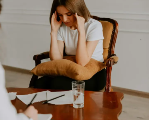Jeune femme assise dans un fauteuil, les mains sur le front, lors d'un entretien avec une thérapeute