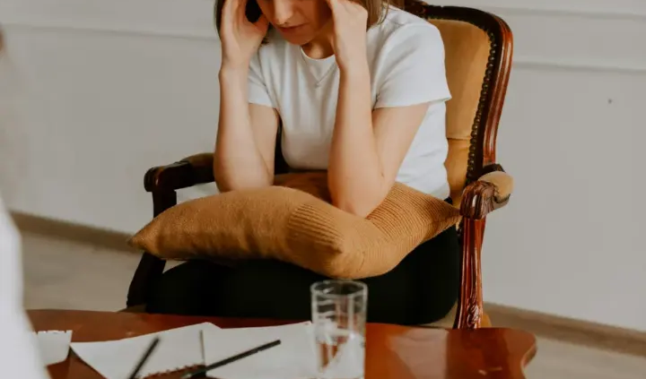 Jeune femme assise dans un fauteuil, les mains sur le front, lors d'un entretien avec une thérapeute