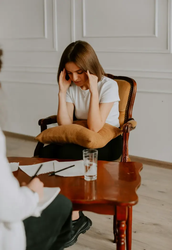 article-stress-720 Jeune femme assise dans un fauteuil, les mains sur le front, lors d'un entretien avec une thérapeute