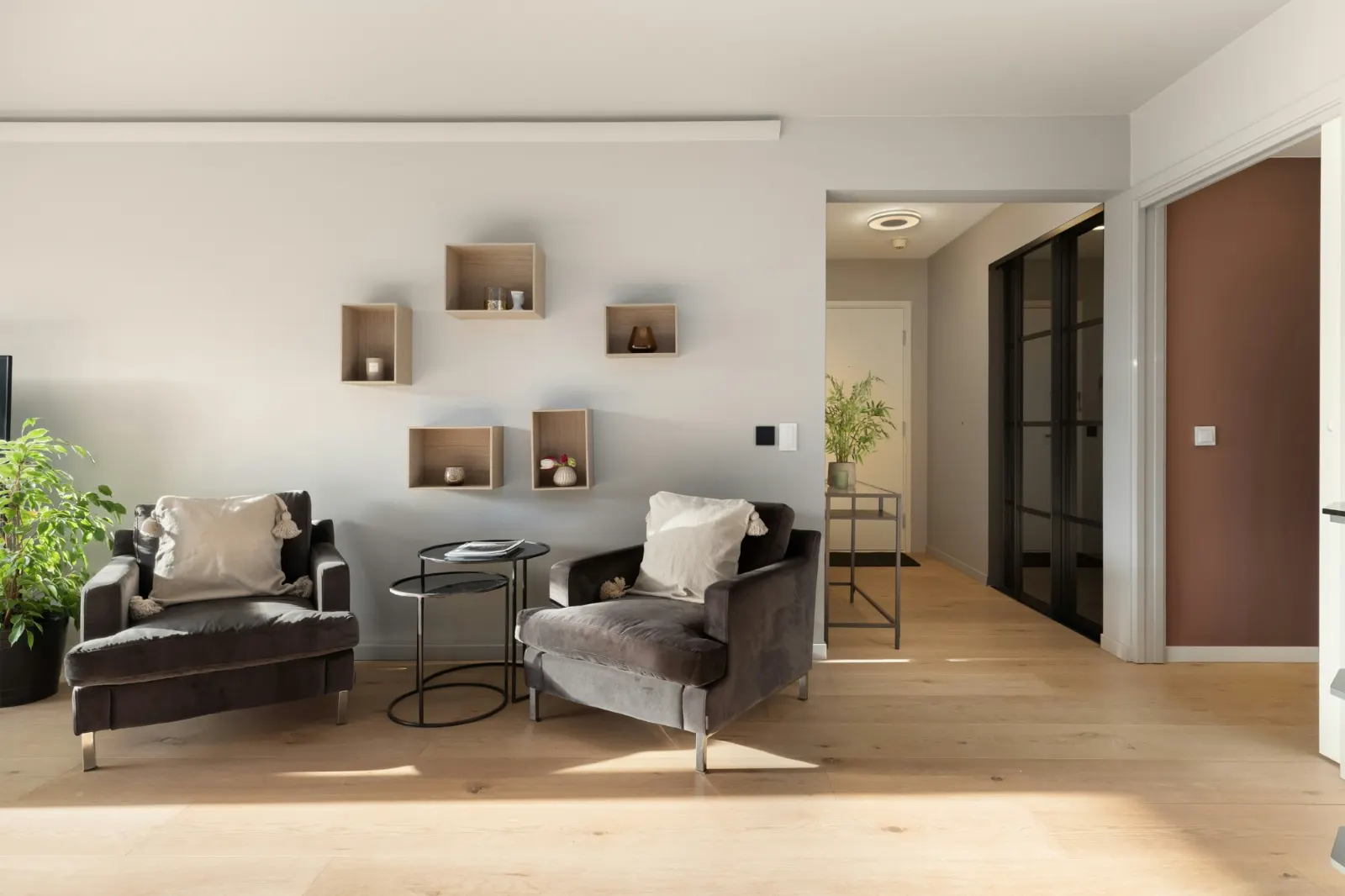 Espace d'accueil du cabinet d'hypnothérapie à Genève : deux fauteuils gris, une table basse et des étagères en bois