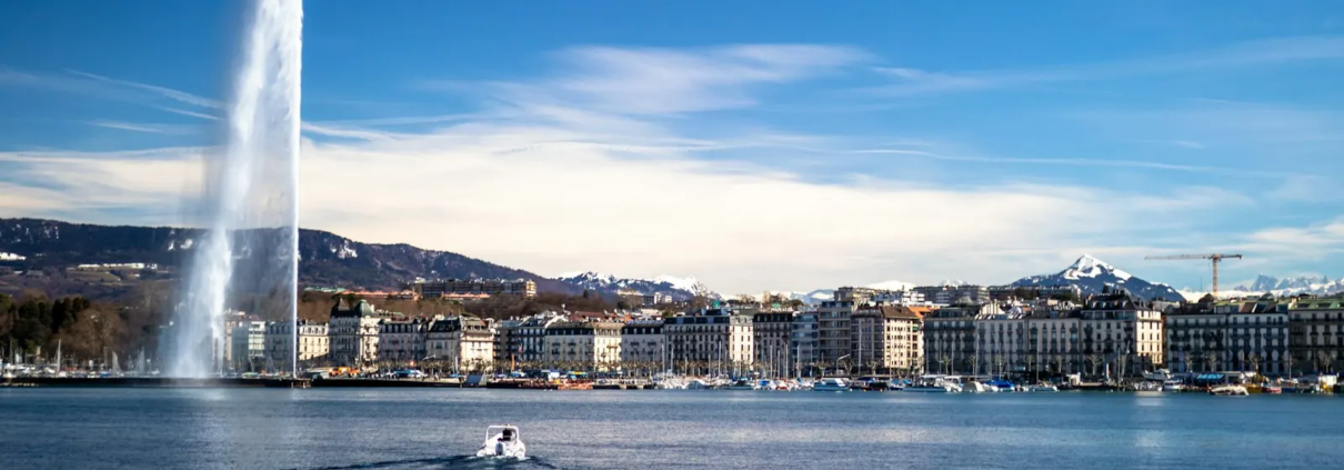 Le Jet d’eau et la rade de Genève sous un ciel bleu, avec les montagnes en arrière-plan