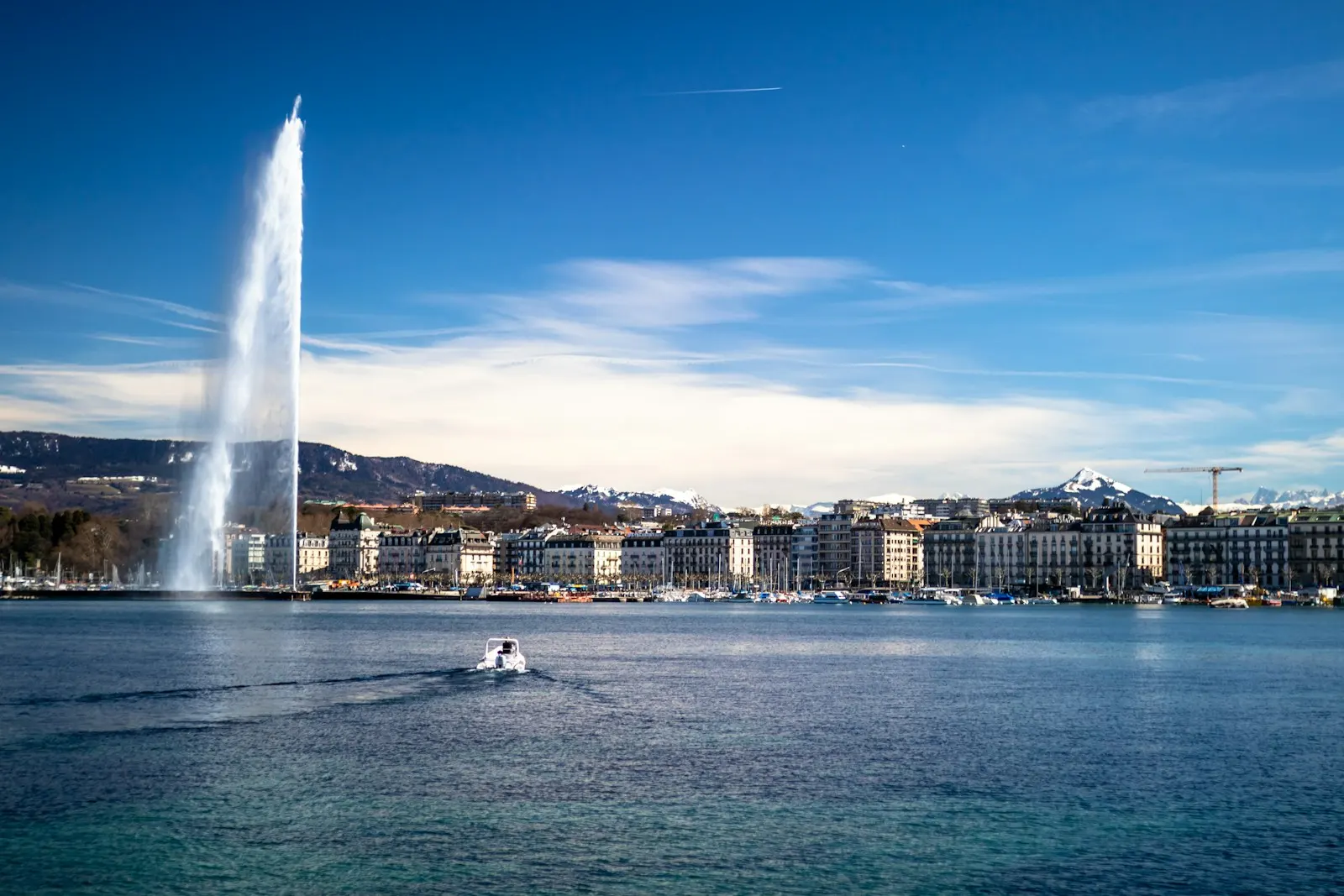 Le Jet d’eau et la rade de Genève sous un ciel bleu, avec les montagnes en arrière-plan